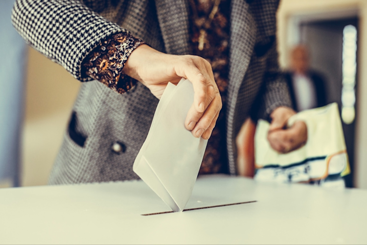 A woman's hand drops a paper ballot into a voting box